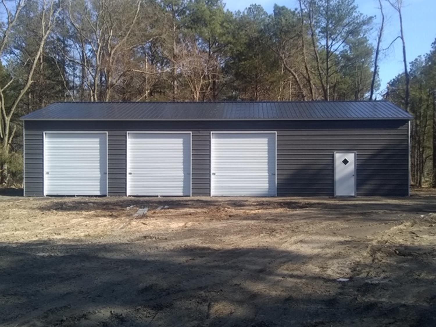 A black garage with white doors is in the middle of a dirt field.
