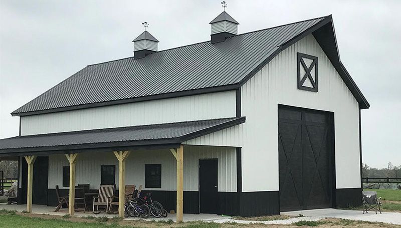 A white barn with a black door and a porch.