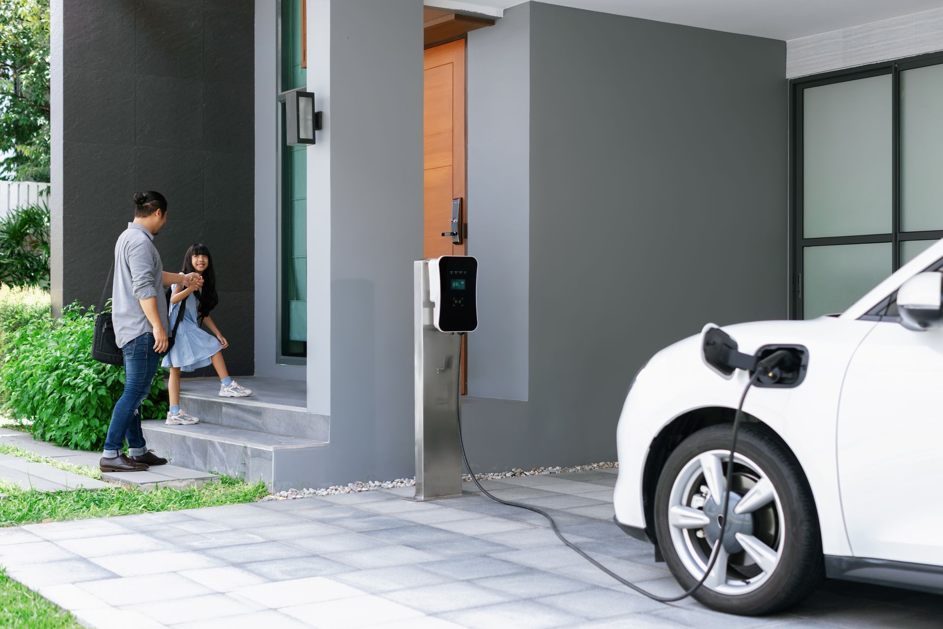 Charging station beside a white electric car, with two people walking by a building entrance.