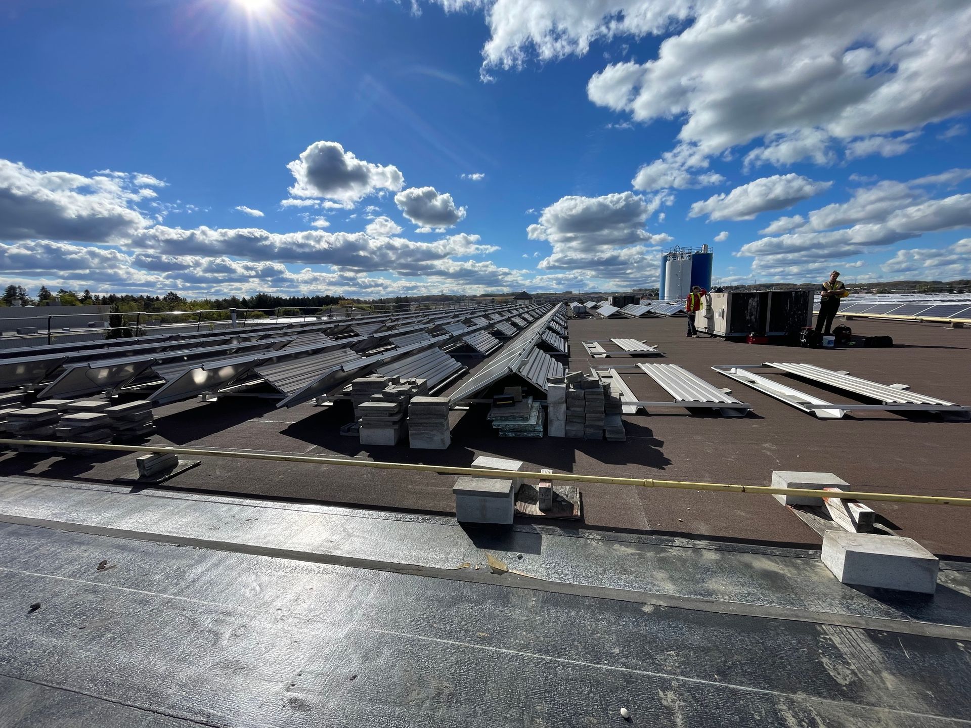 Rooftop under construction with black roofing materials, bright blue sky, and scattered clouds.