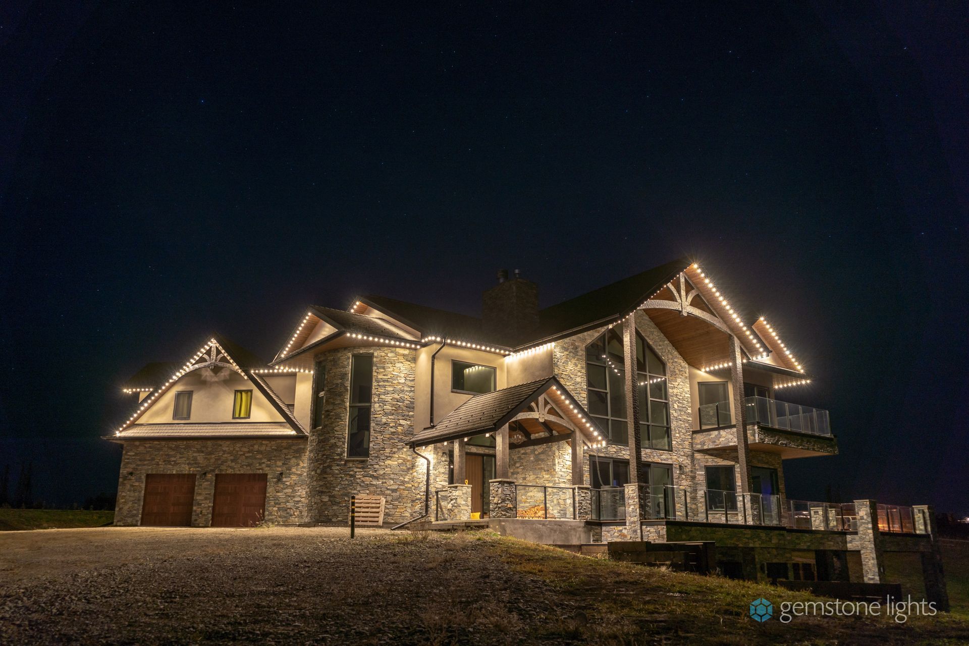 Large stone house with warm exterior lights at night, including a garage and balcony.