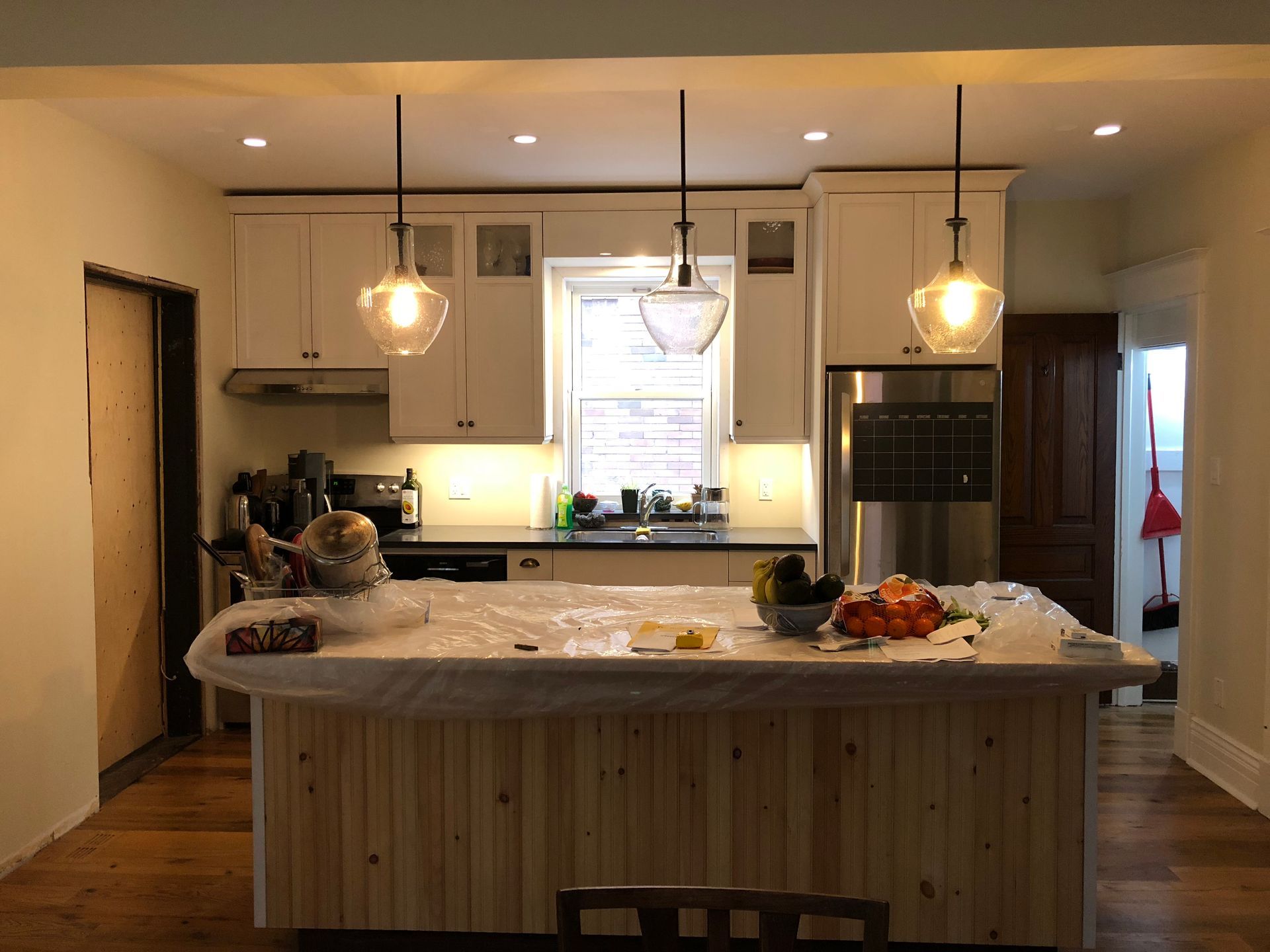 A kitchen island with unfinished pine paneling stands before white cabinets, stainless steel appliances, and lighting.