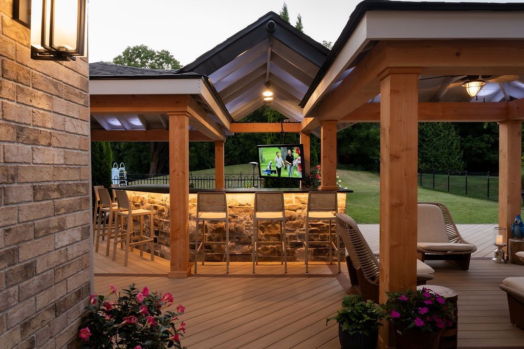 Outdoor covered patio with wood beams, stone wall, and dining tables overlooking a pool at dusk
