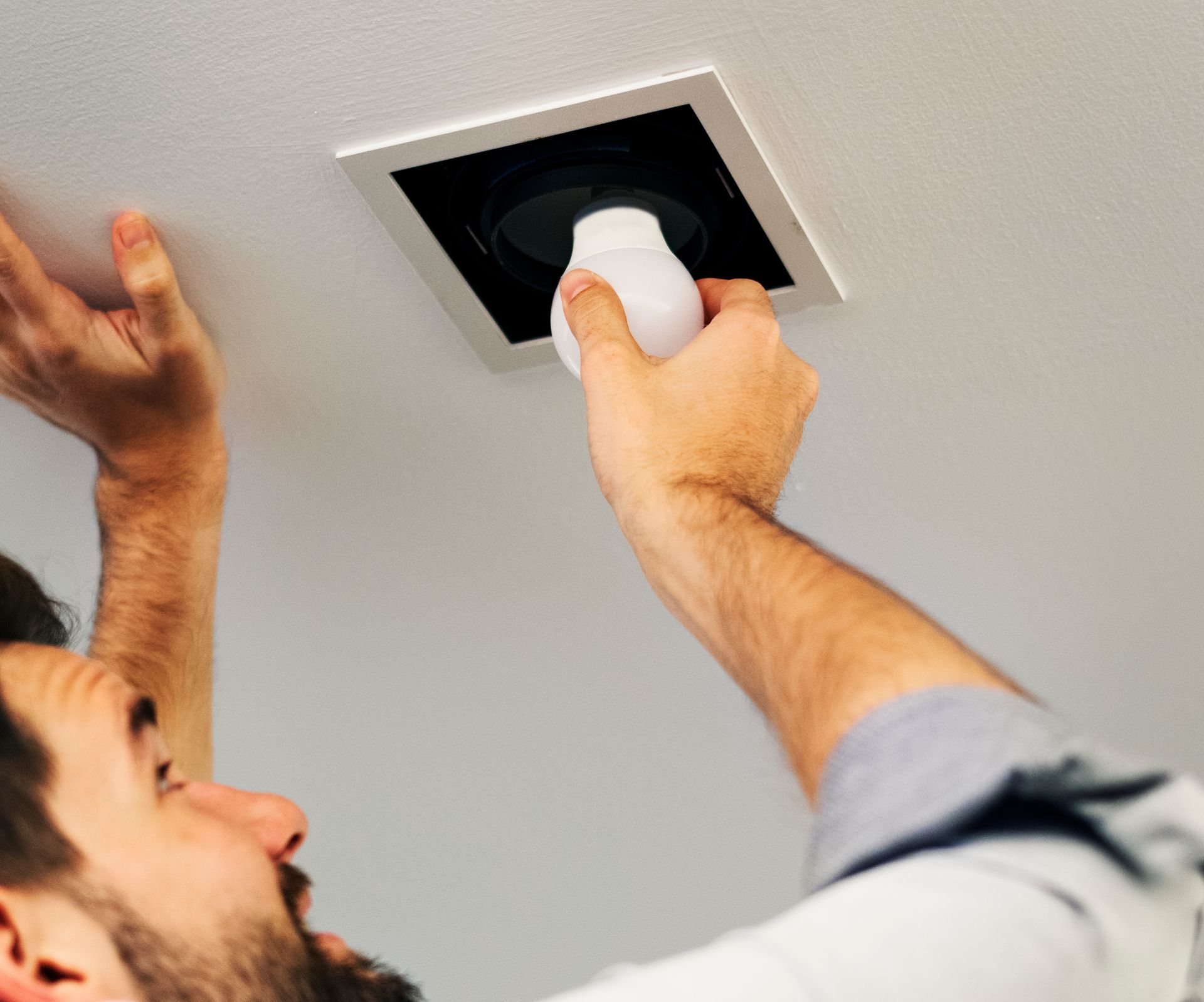 A man is installing a light fixture in a ceiling