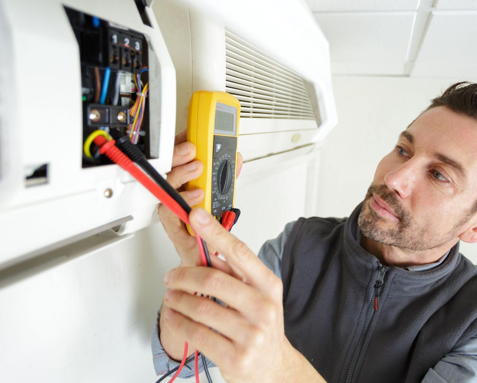 A man is working on an air conditioner with a multimeter.