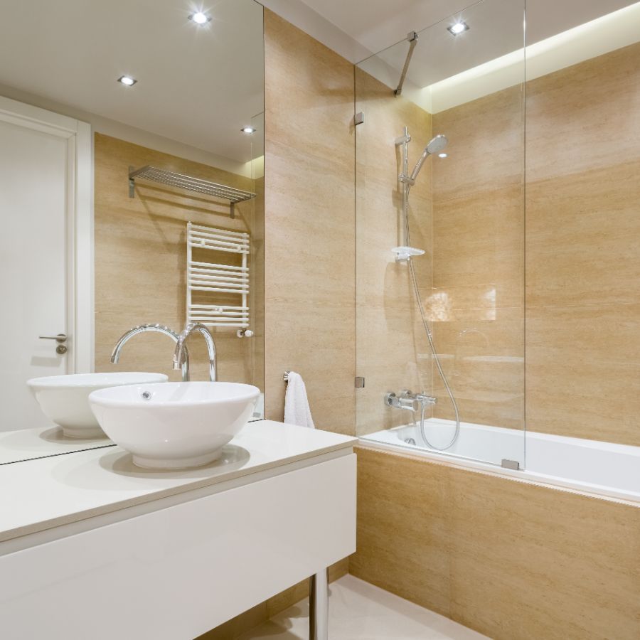 Bagno moderno con piastrelle beige, doccia in vetro, portasciugamani a parete e mobile lavabo bianco.