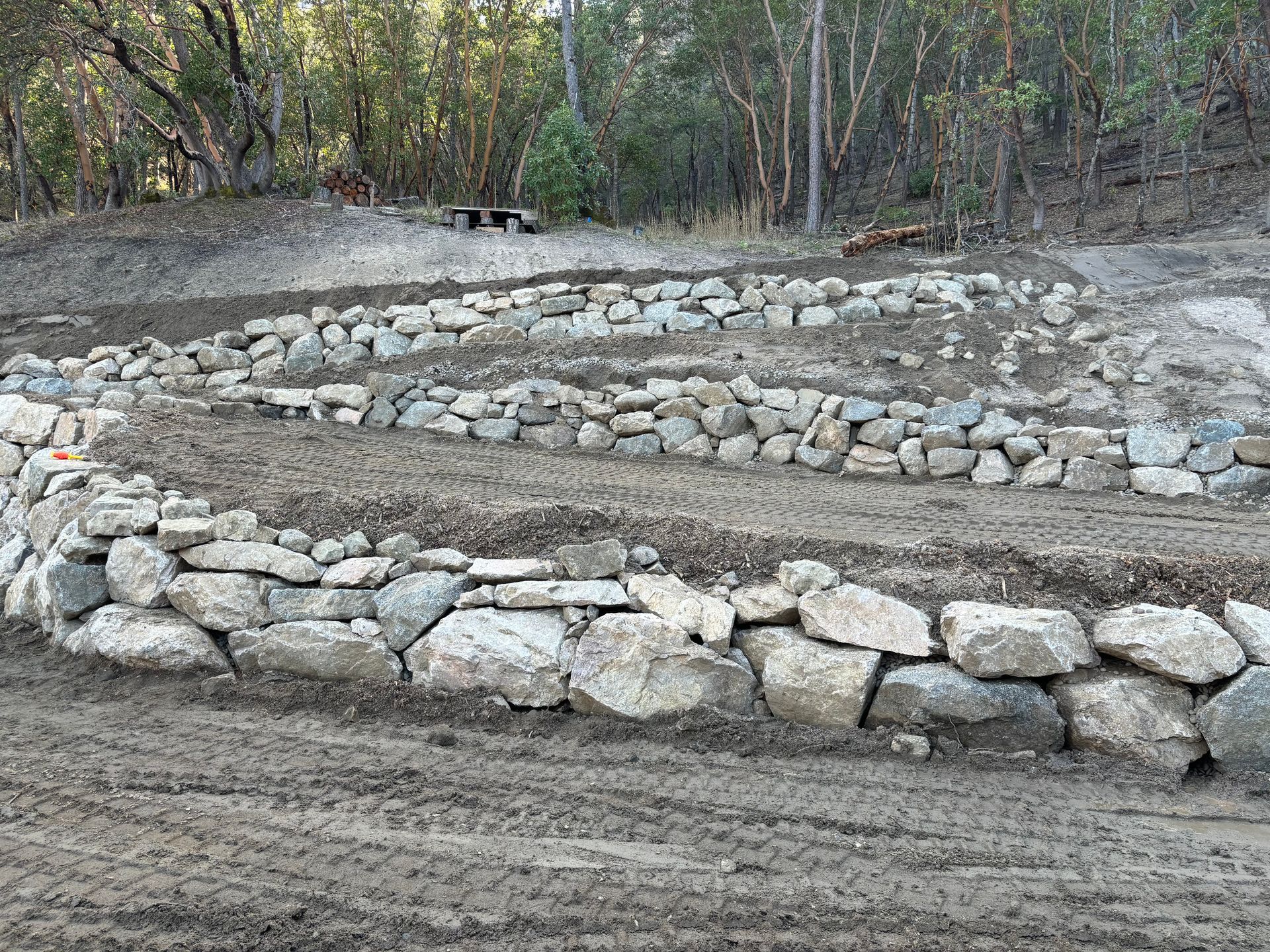 A driveway is being constructed with a rock retaining wall to go up a slope of a hill