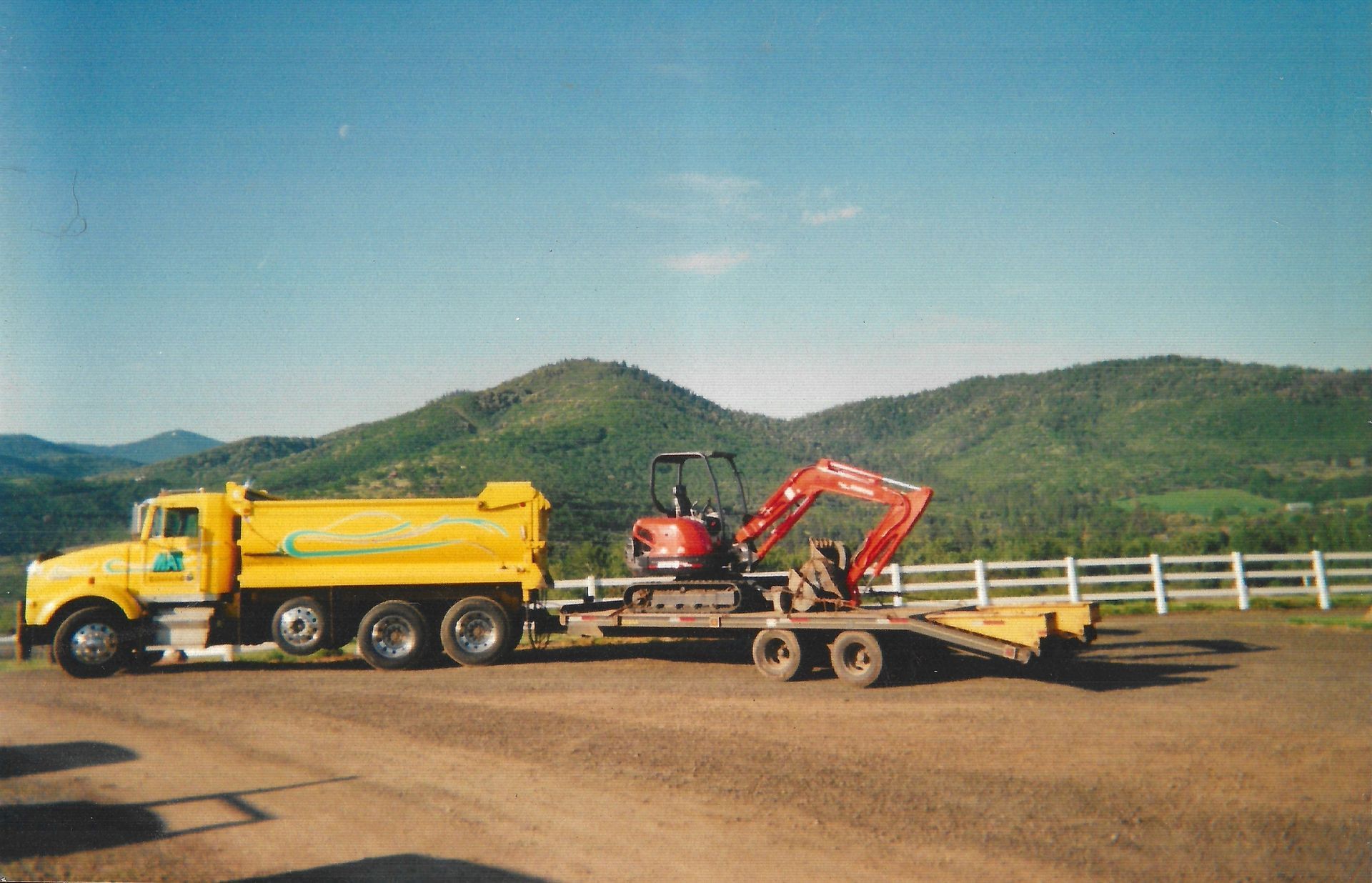 A yellow truck is carrying a red excavator on a trailer in Ashland, Oregon.