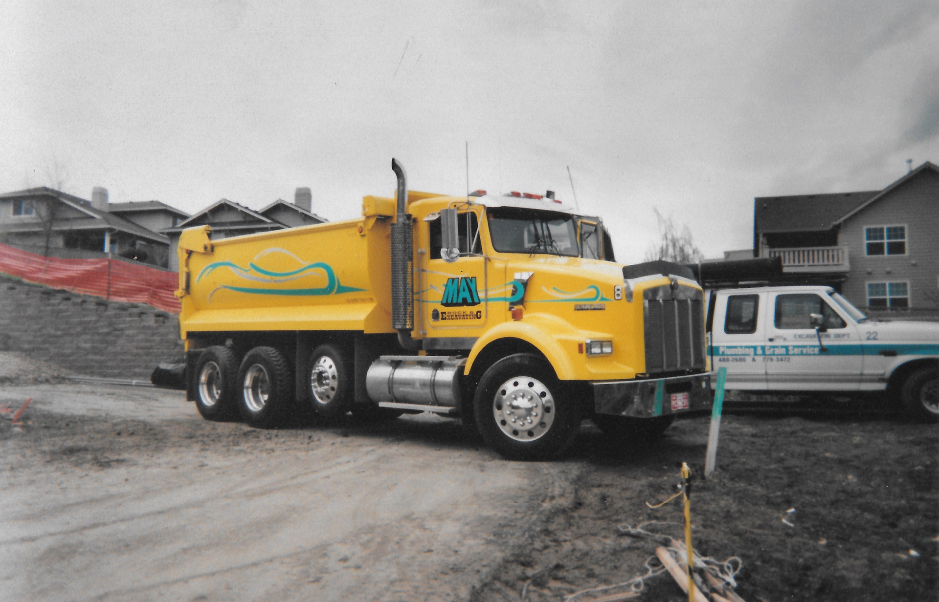 A yellow dump truck is parked next to a white truck