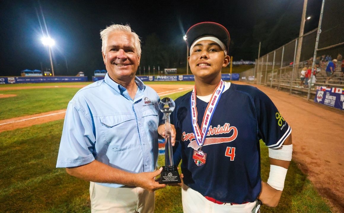 Two men on a baseball field, one holding a trophy, under stadium lights at night