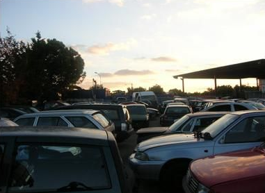 Automobili ammucchiate in uno sfasciacarrozze, di vari colori e stili, con alcune parti mancanti.