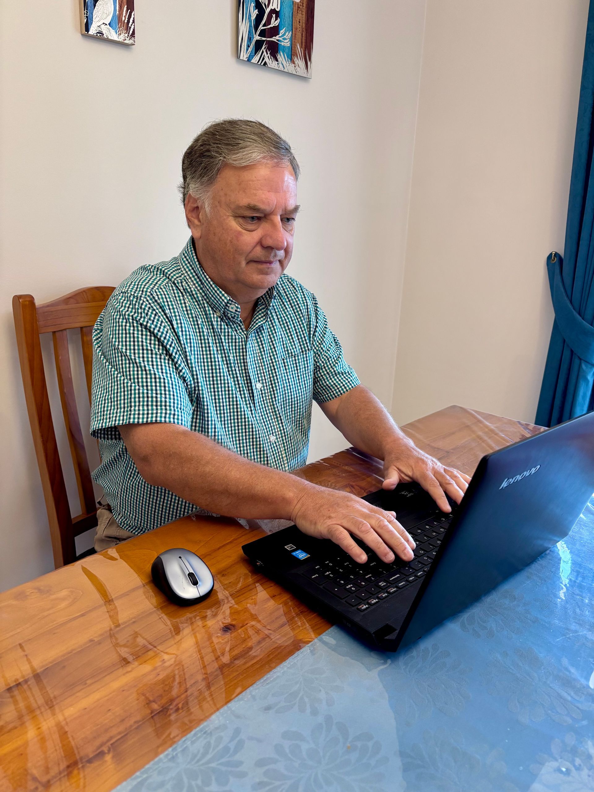 Man seated at a wooden table using a laptop and mouse in a home setting