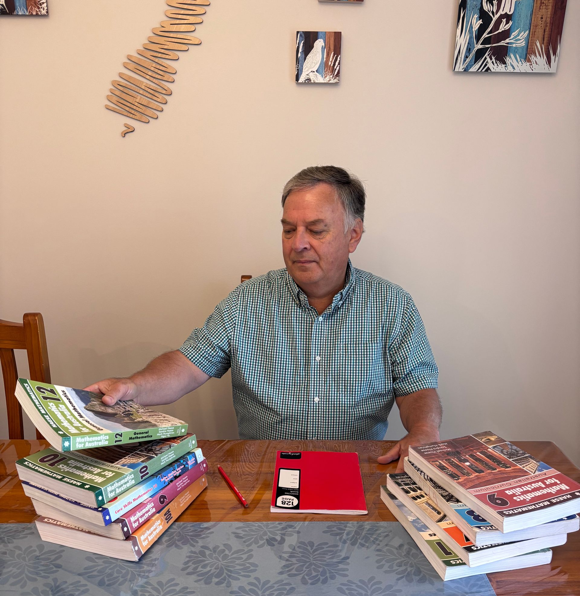 Man seated at a table reading a book beside two stacks of books, with a red notebook in front of him.
