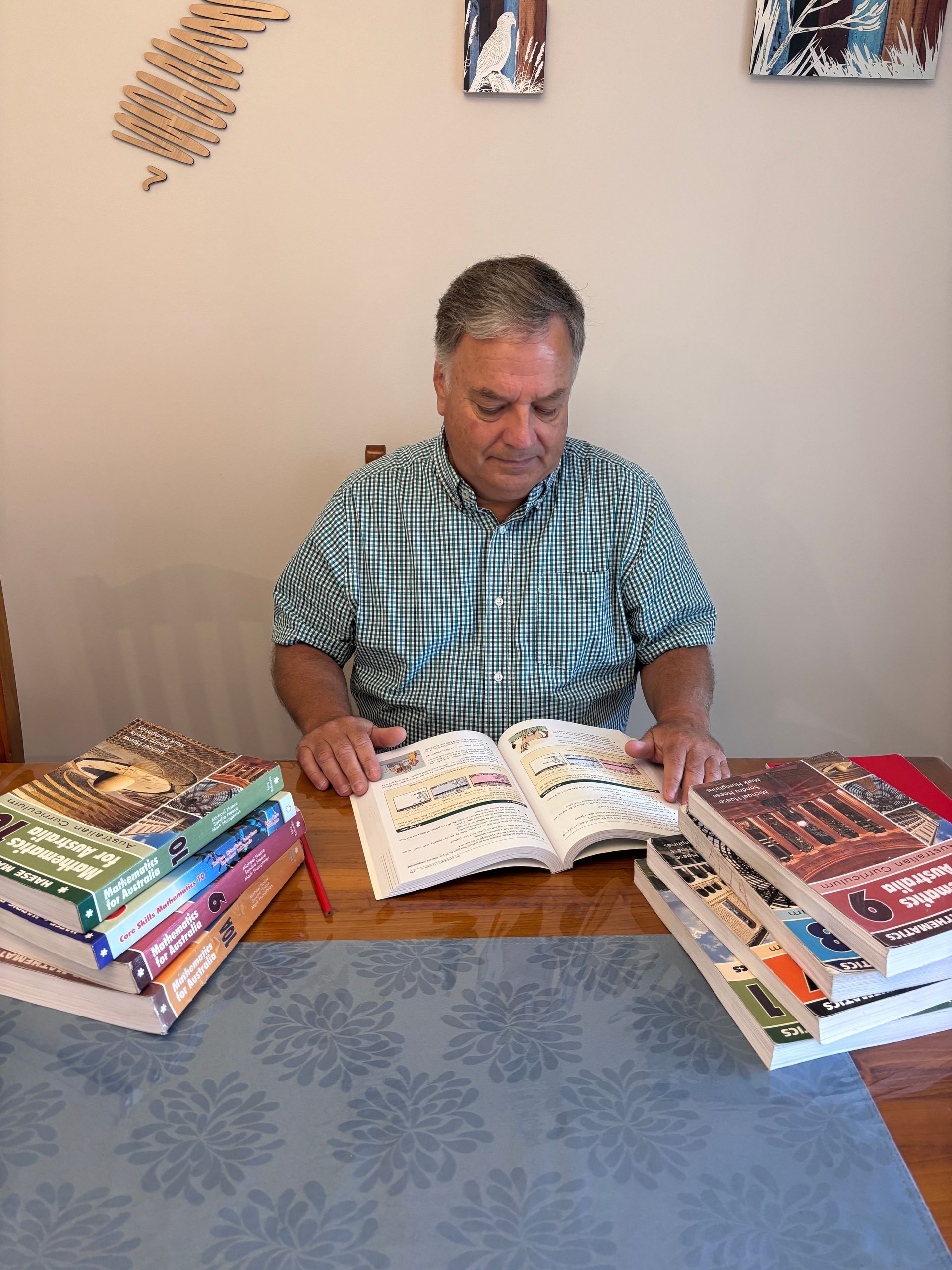 Man reading an open book at a table, surrounded by stacks of colorful books