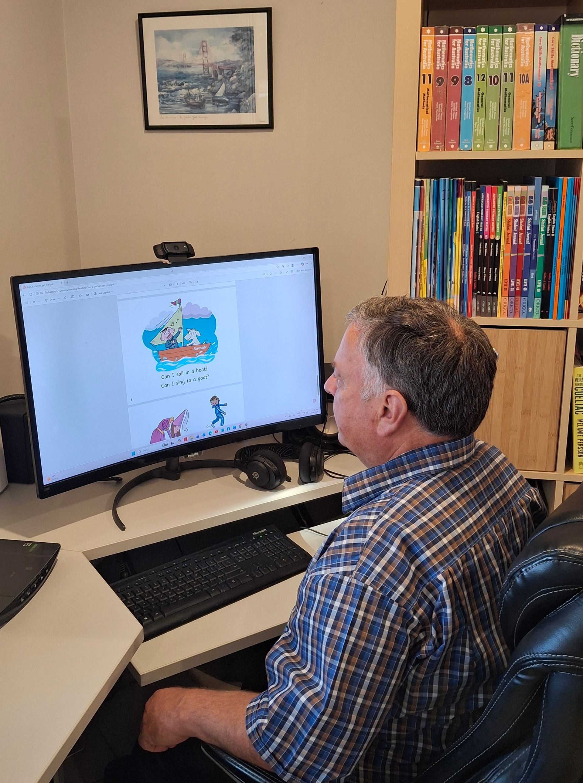 Person seated at a desk using a desktop computer in a home office with bookshelves nearby.