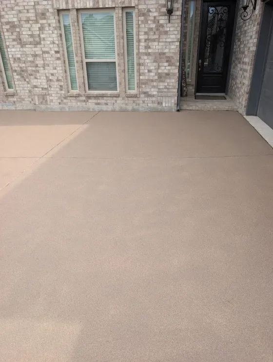 Beige concrete patio beside a brick house, with a window and front door visible.