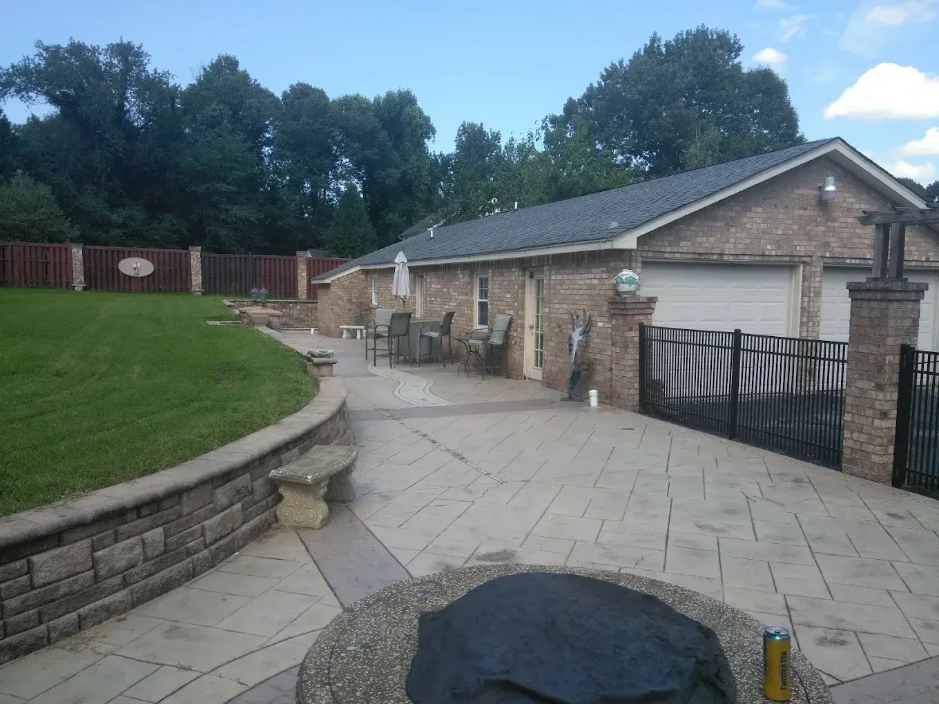Stone driveway and garage beside a curved lawn, with patio furniture and a black gate in front.