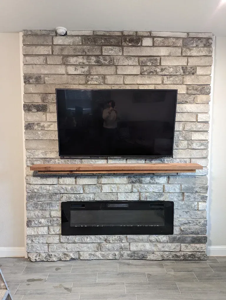 Living room fireplace wall with mounted TV, wood mantel, and gray stone brick surround