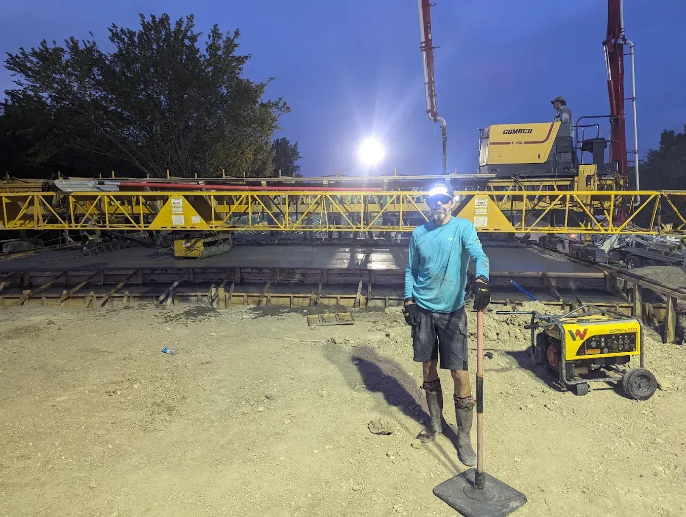 Construction worker walking toward a yellow crane at night under bright lights