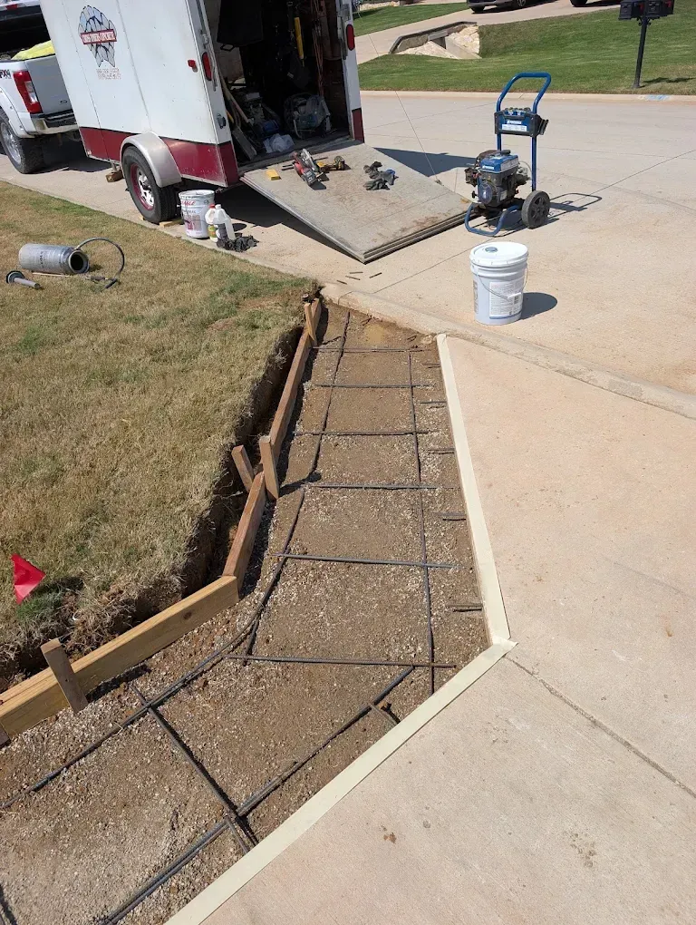 Sidewalk repair with fresh concrete forms and rebar beside a work truck on a residential curbside.