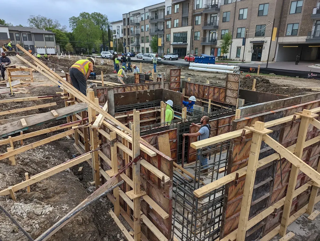 Workers building concrete foundation forms at an apartment construction site, with rebar and wooden supports.