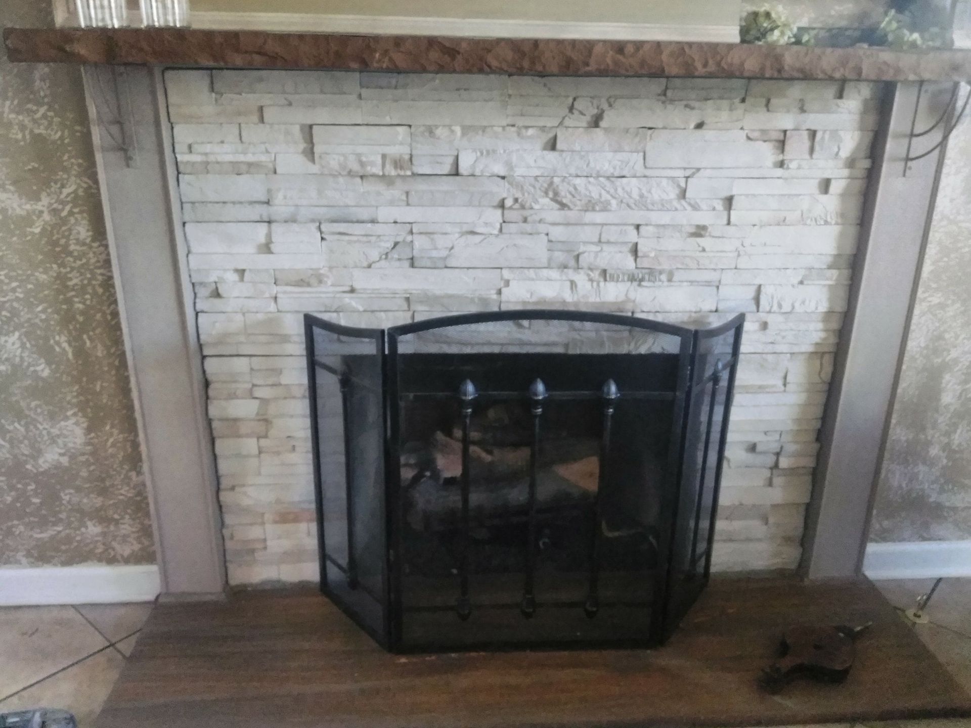 Fireplace with white brick surround, wood mantel, and black metal screen in a tiled room.