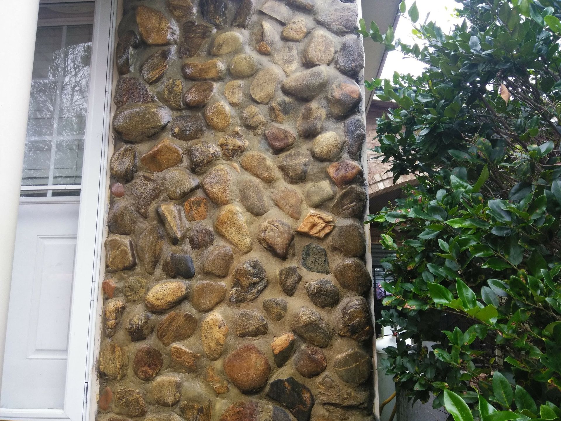 Close-up of a stone wall beside a white door and green shrubbery.