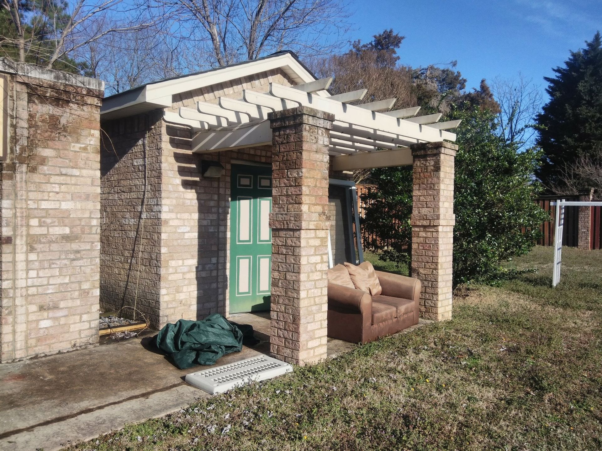 Abandoned porch with green door, stone columns, and a couch on the grass beside it