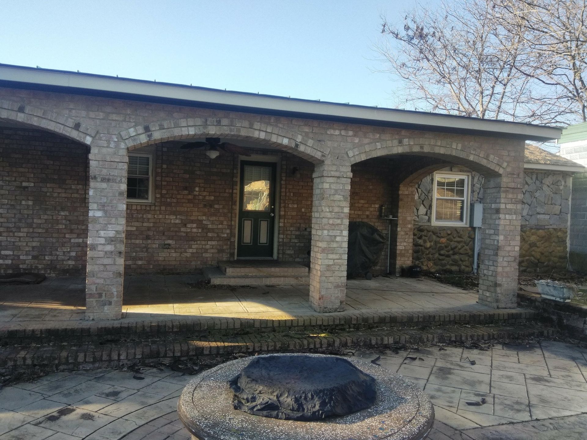 Brick house porch with arched columns and a central front door, viewed from the yard.