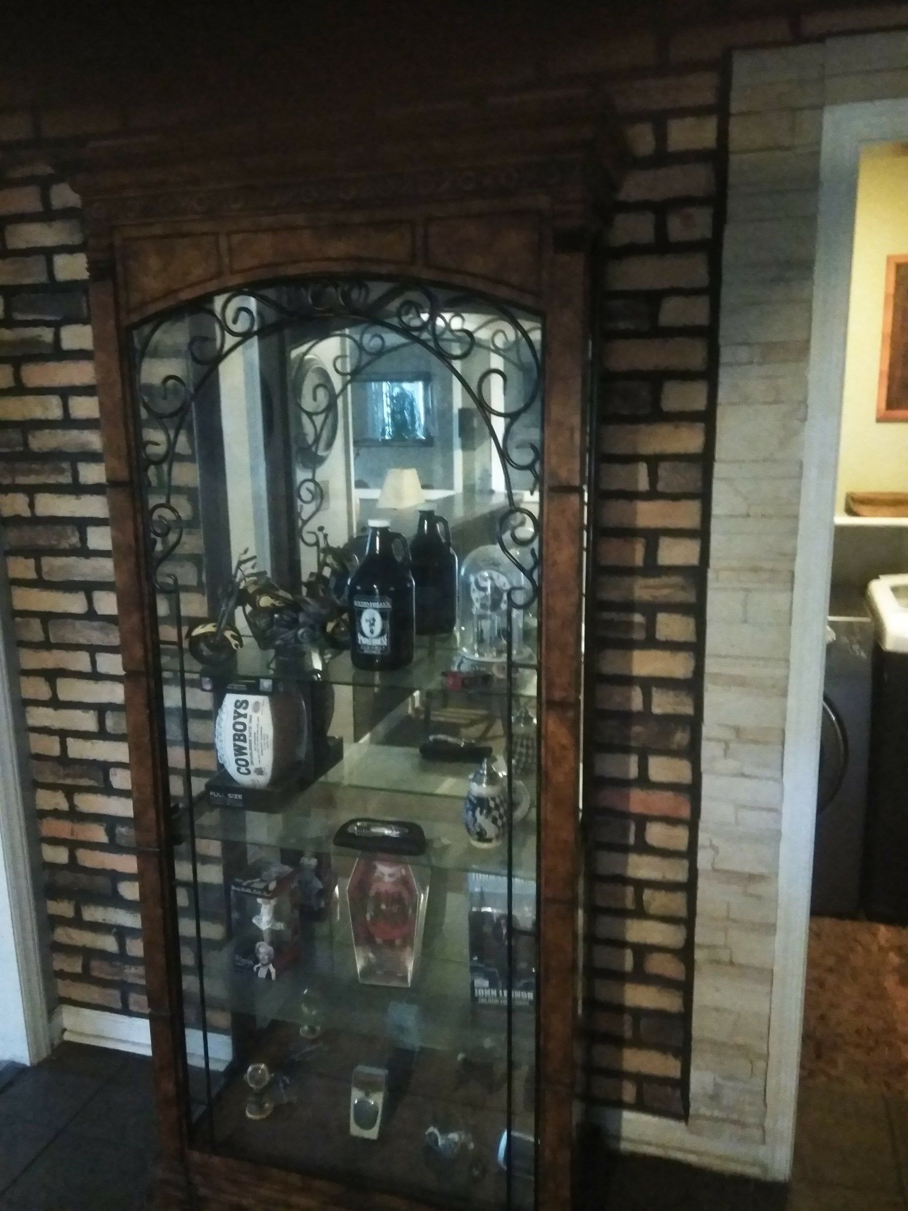 Glass-front display cabinet with decorative wrought-iron trim in a brick wall niche