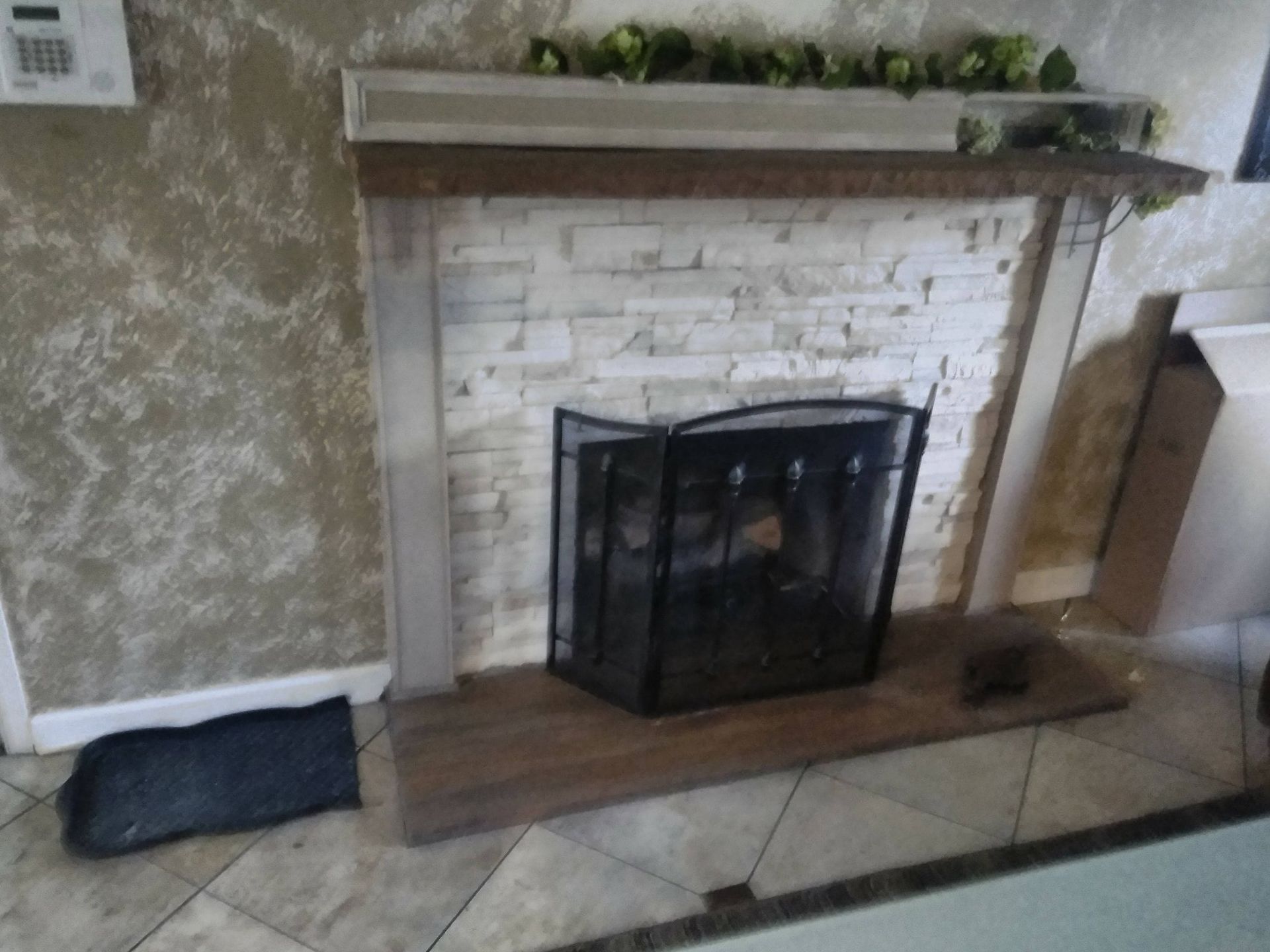 White brick fireplace with black screen, wooden mantel, and tiled hearth in a living room