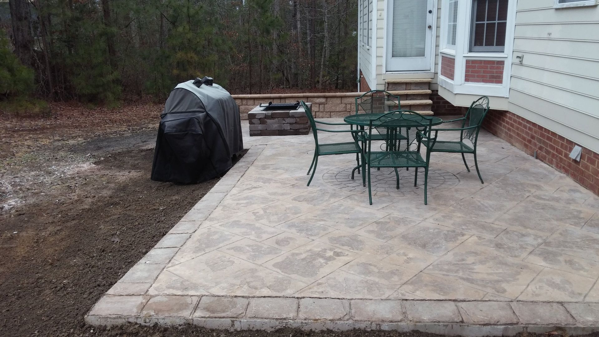 Back patio with patio set and covered grill beside a house and wooded yard