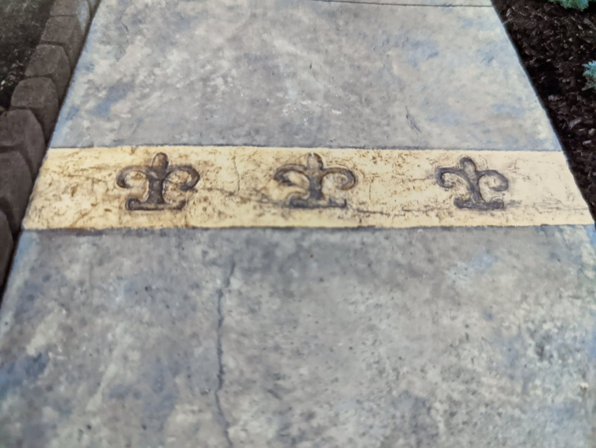 Stone walkway with a pale strip decorated by three fleur-de-lis symbols