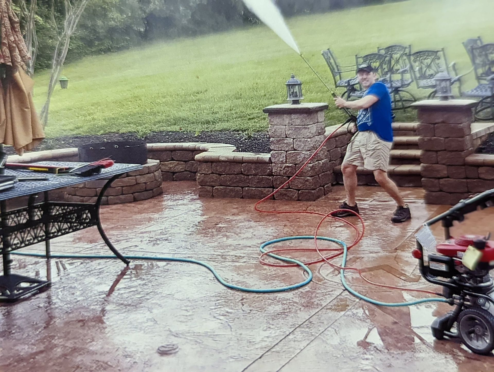 Person pressure-washing a wet brick patio in the rain, with chairs and a hose nearby.