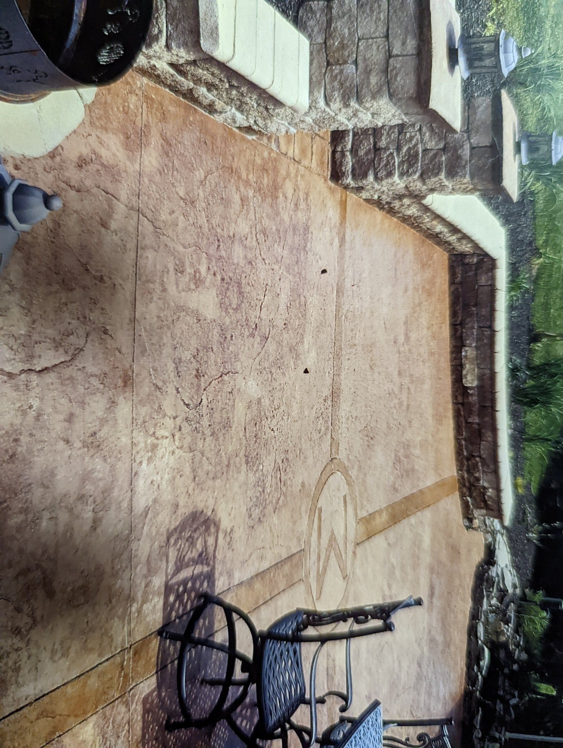 Small black-and-white wheelchair on a paved patio beside a stone wall and garden border.