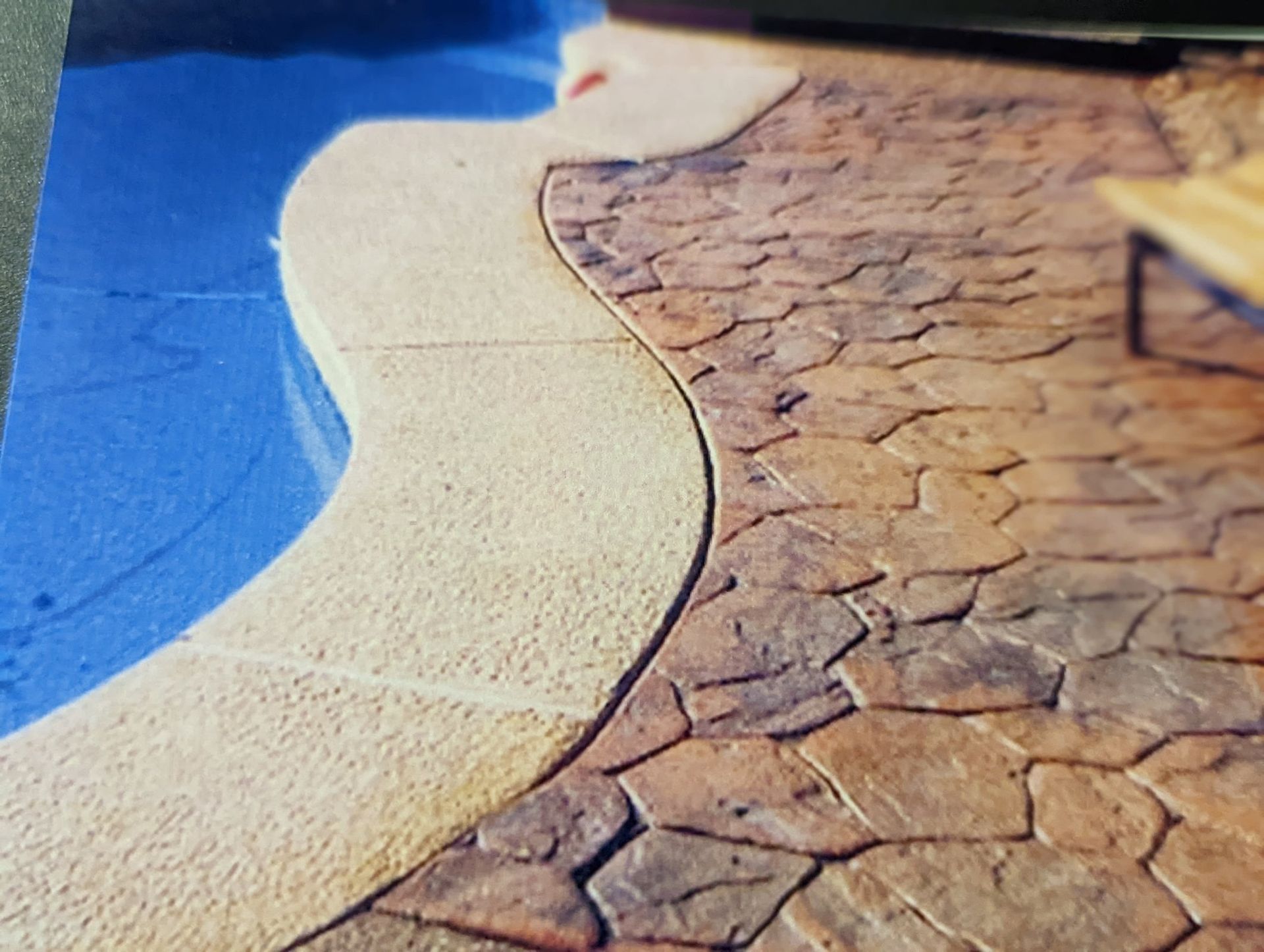 Curved beige walkway beside blue water and cracked brown ground textures