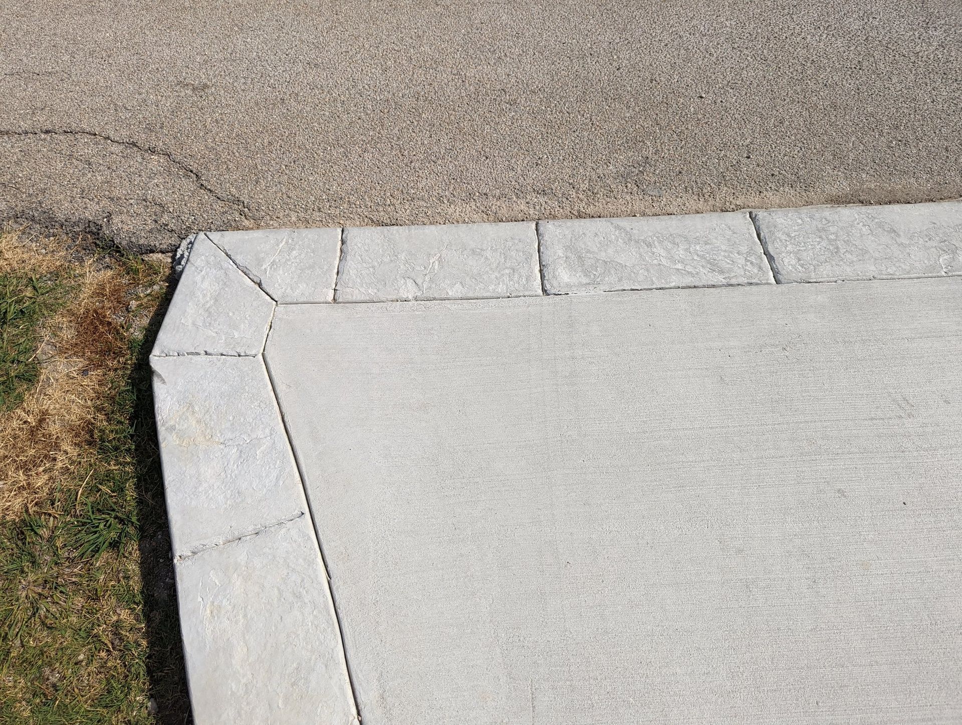 Concrete sidewalk corner with beveled edges beside a strip of brown grass