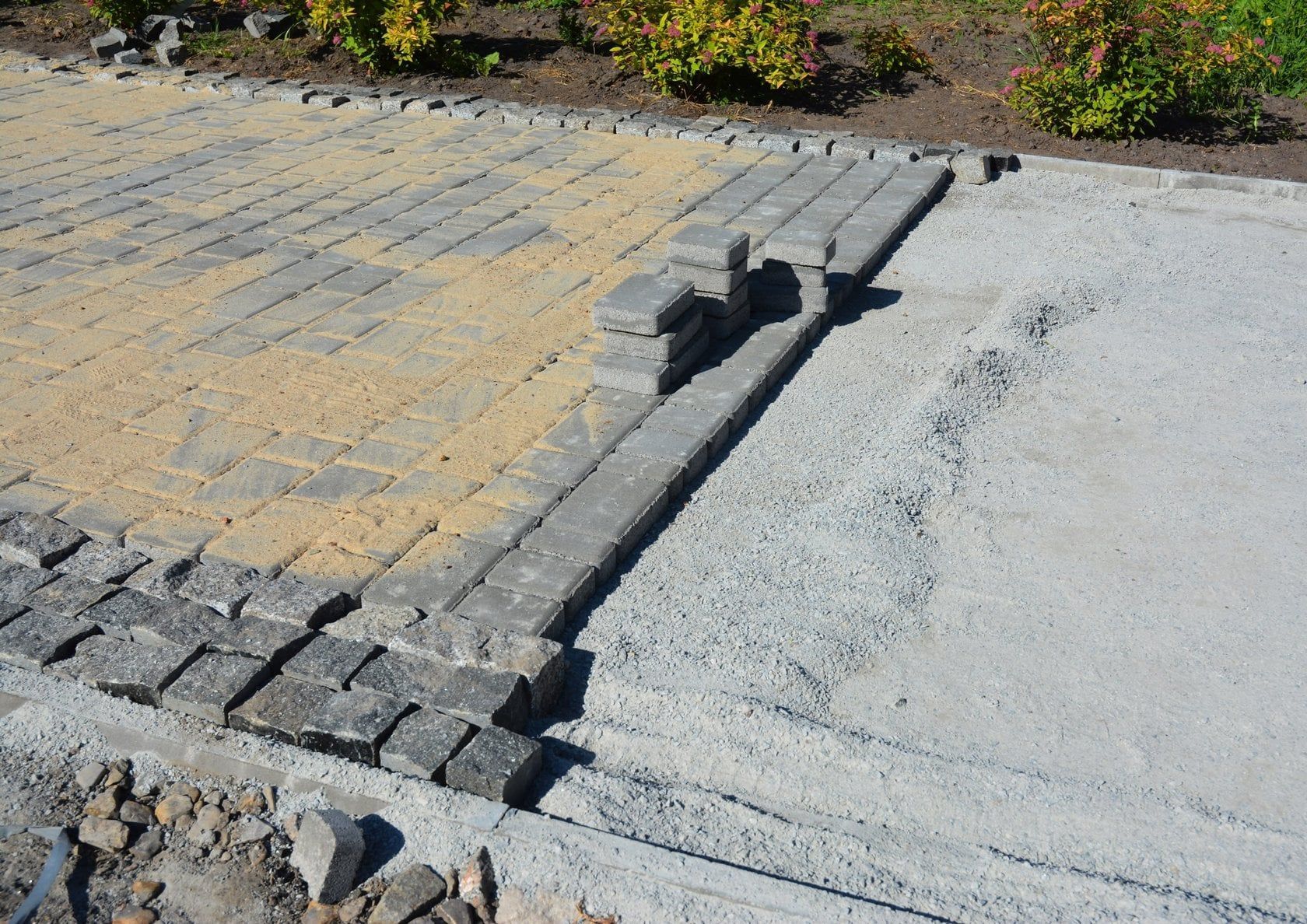Paver walkway and curb edge transitioning to a gravel surface beside shrubs