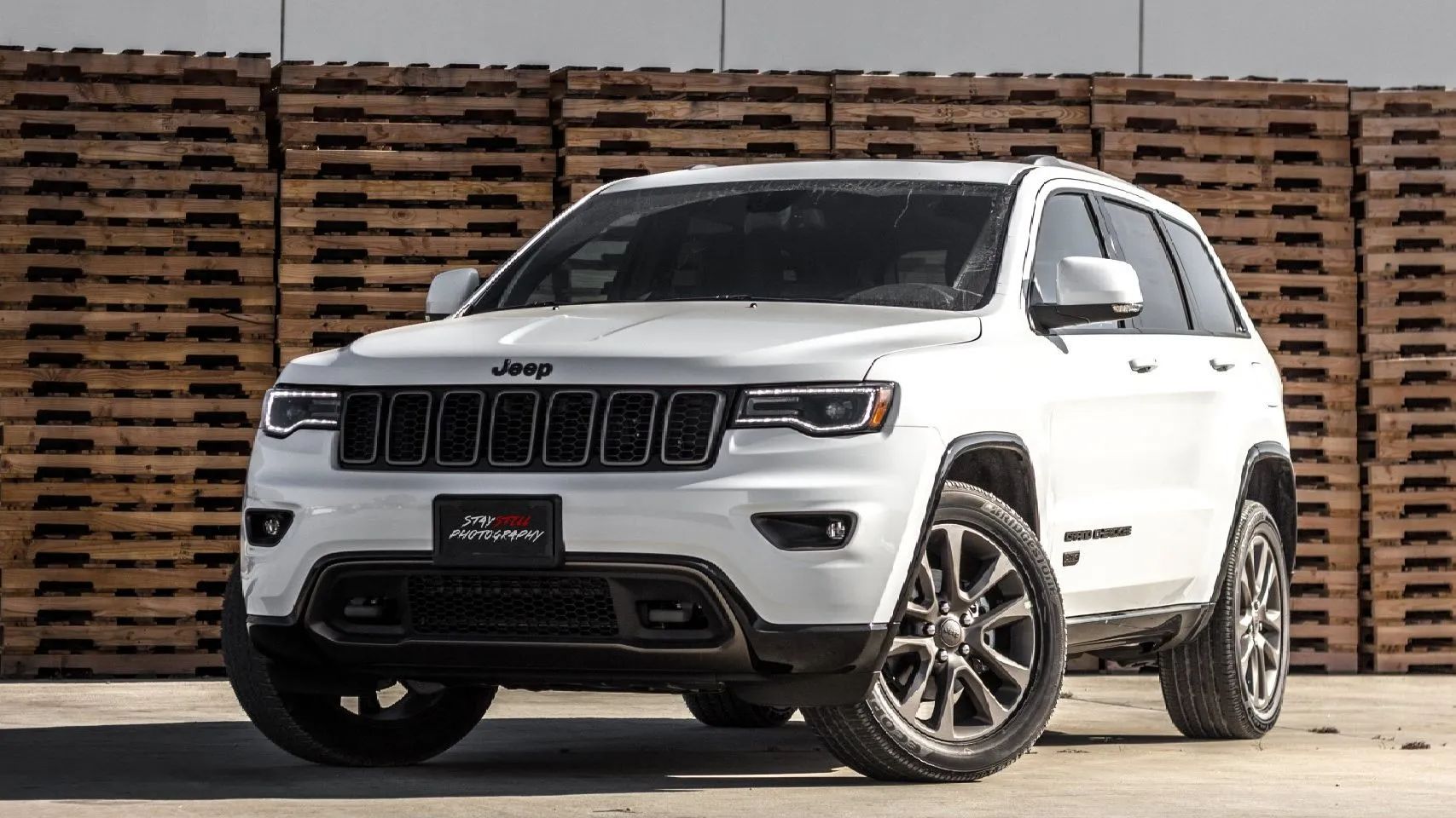 White Jeep Grand Cherokee SUV with black accents parked in front of wood pallets.