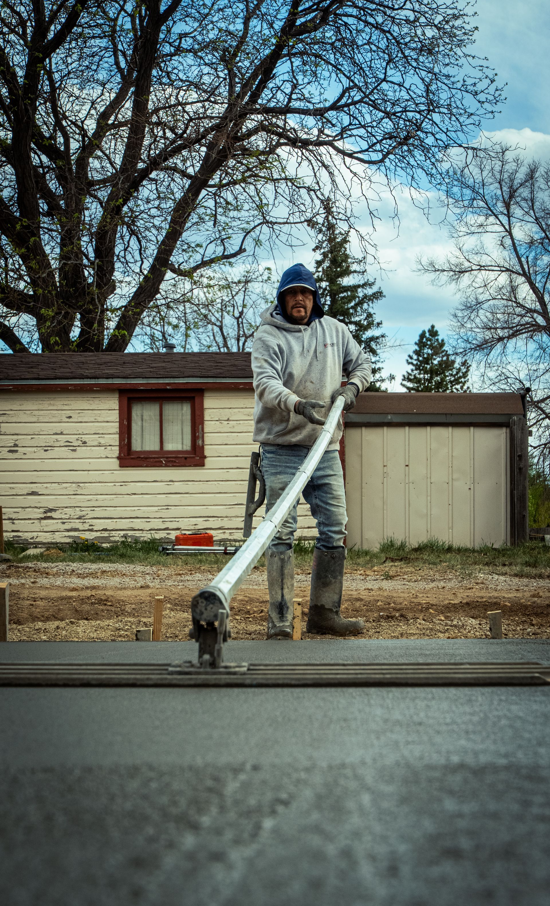 Person with a leaf blower clearing leaves on a roadside in front of a house