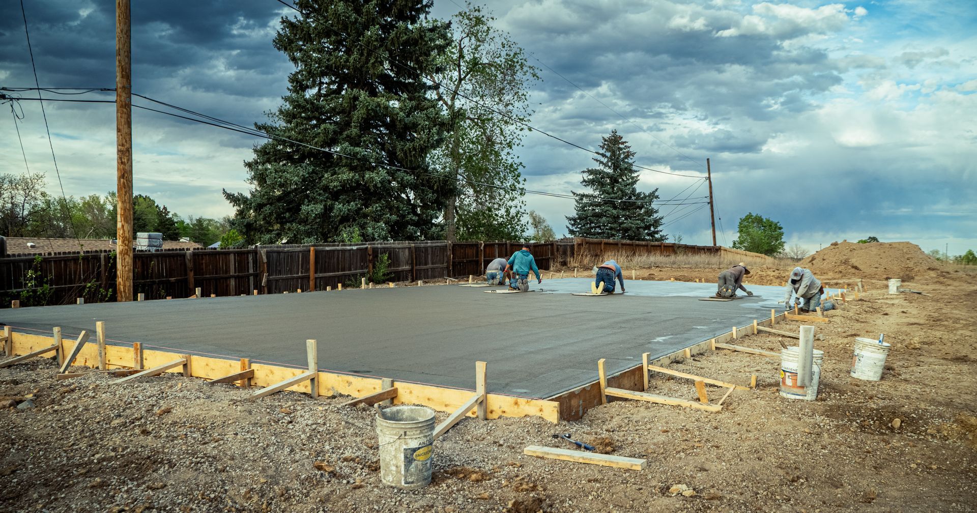 Concrete foundation being poured at a construction site under a cloudy sky