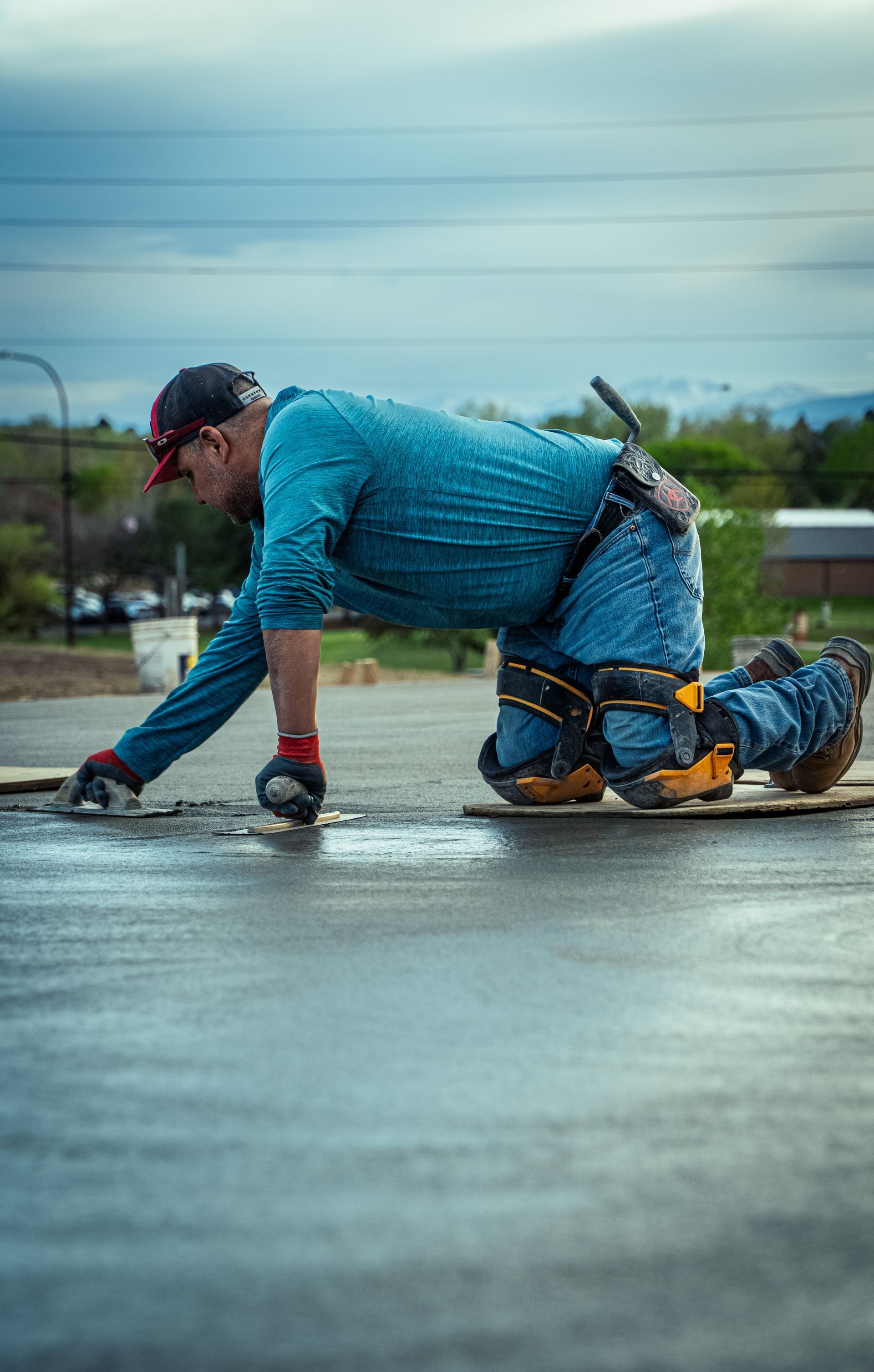 Kneeling cyclist in blue gear on wet pavement under cloudy skies, one hand on the ground.