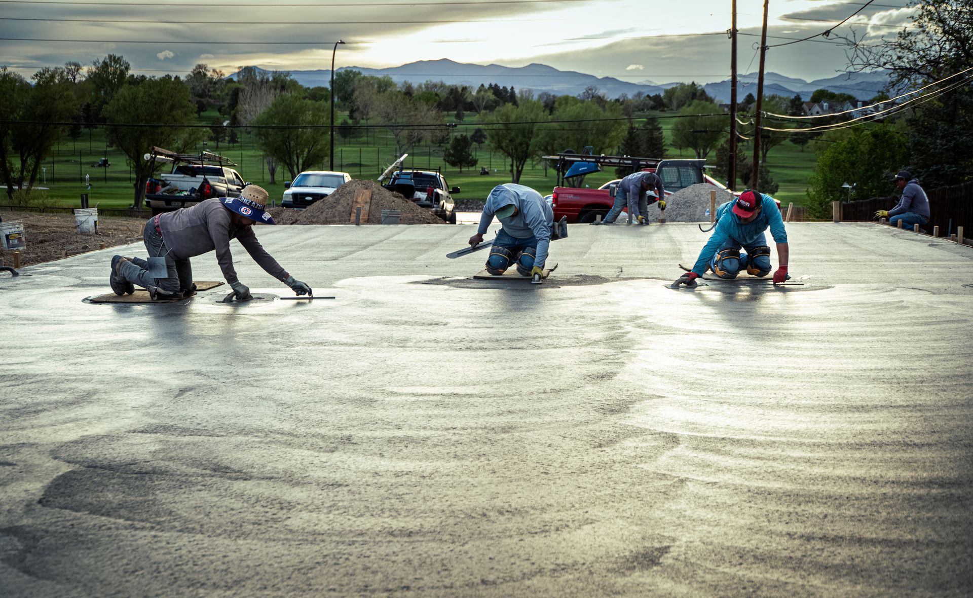 Workers smoothing wet concrete at an outdoor construction site with mountains in the background