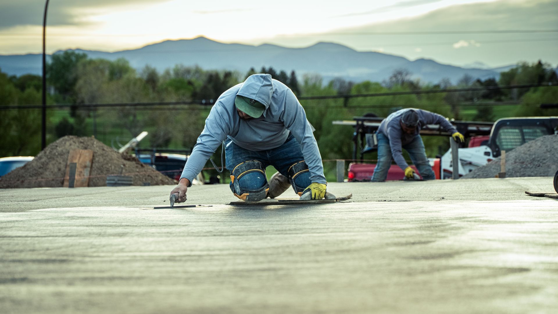 Workers troweling a wet concrete slab at a construction site with mountains in the background