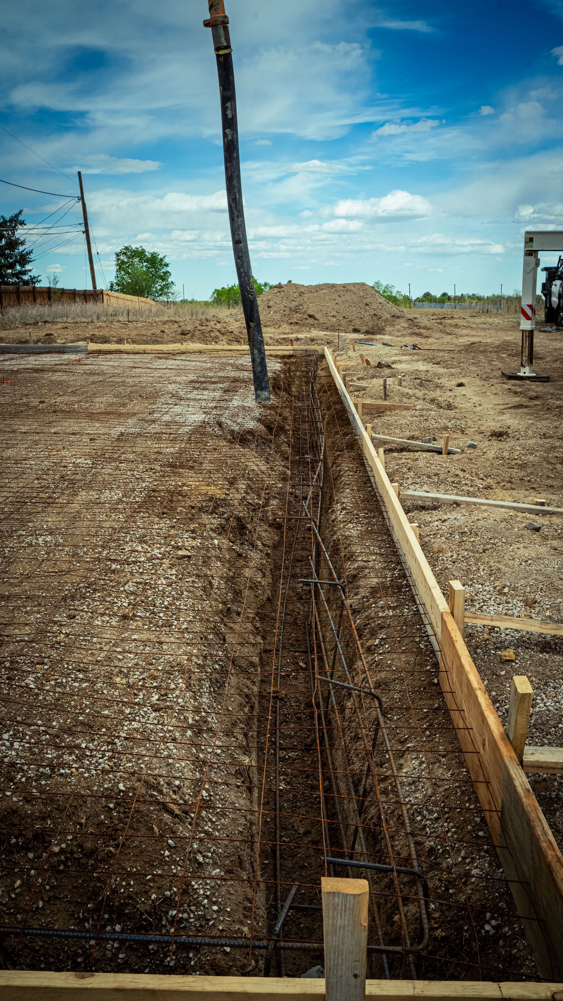 Trenched gravel path bordered by wooden forms under a blue sky on a construction site