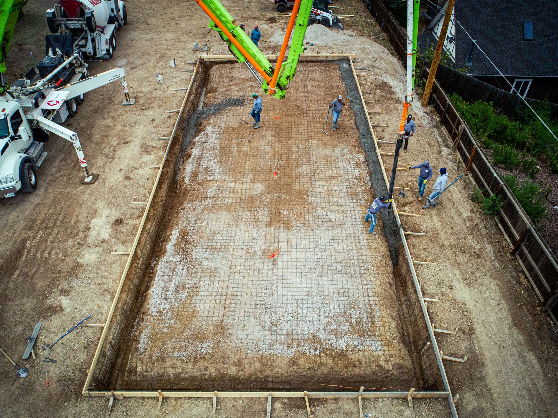 Construction site with concrete foundation slab, workers, and a concrete pump arm overhead