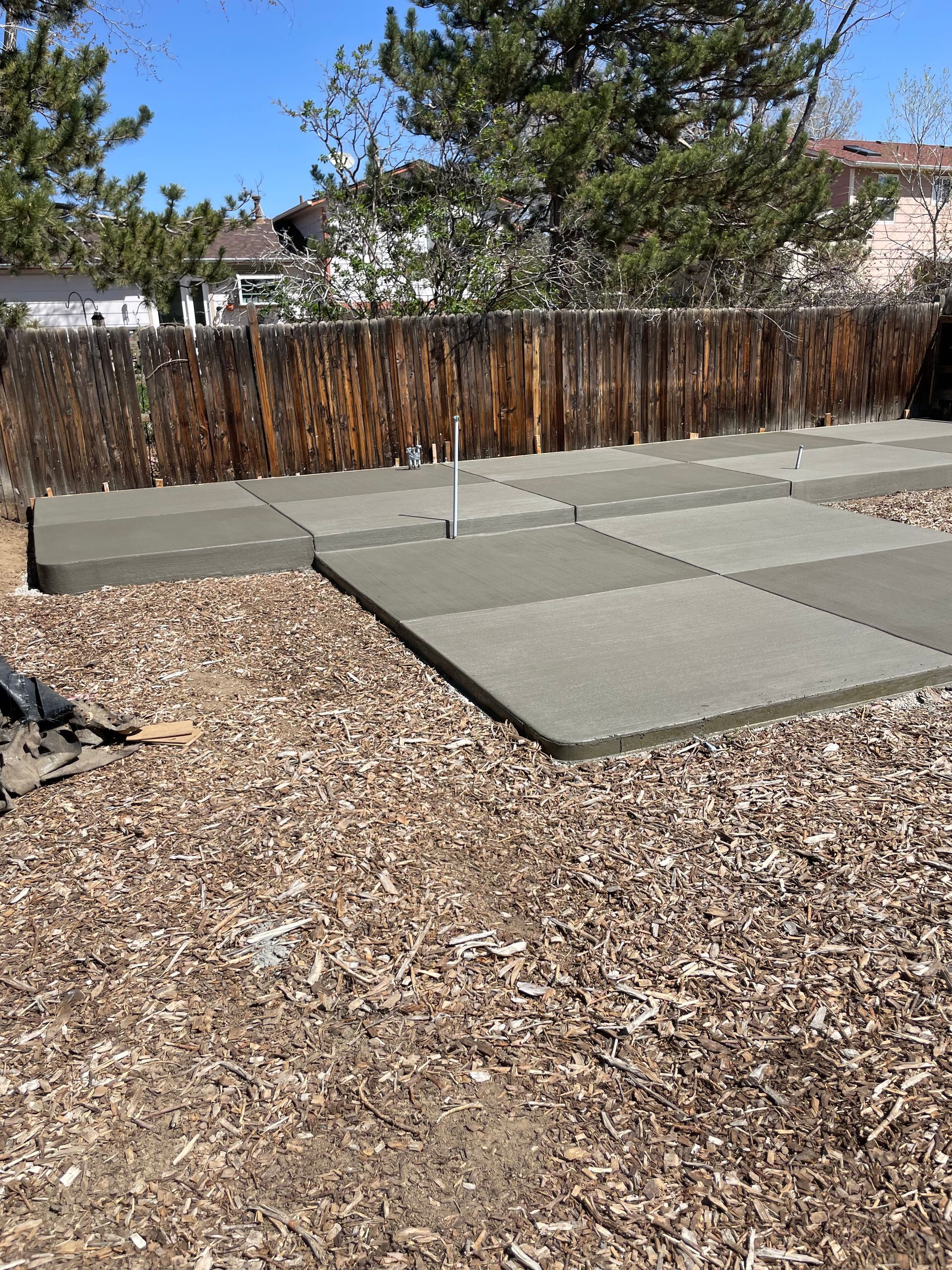 A concrete walkway is being built in a backyard with a wooden fence in the background.