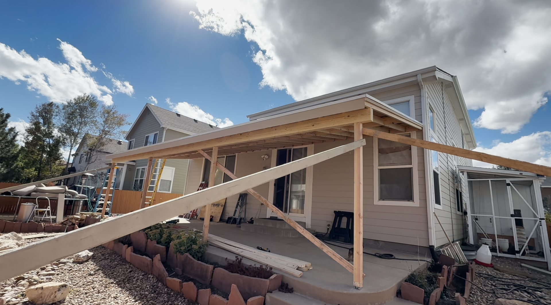 Partially renovated house with wooden framing, white siding, and a front porch under a bright blue sky