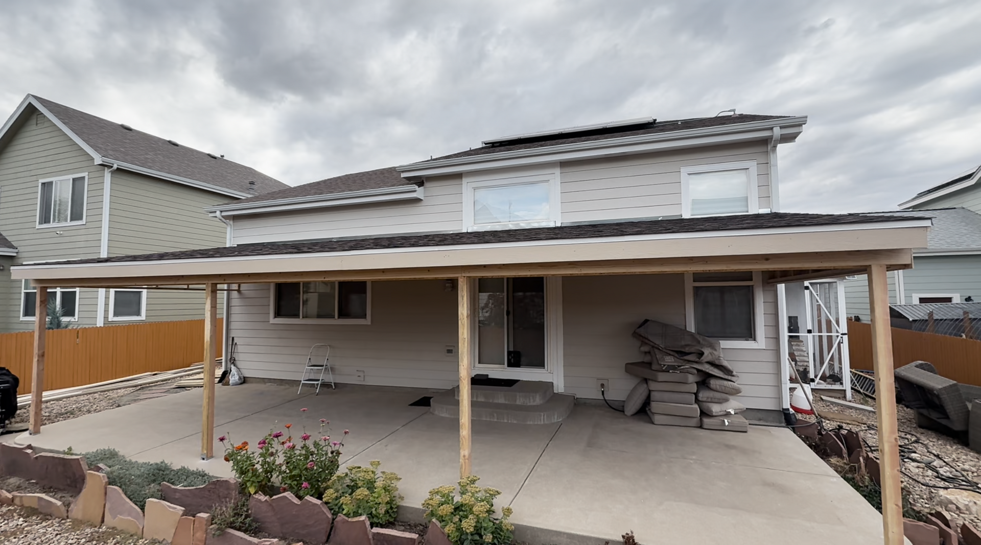Suburban house with a covered patio and stacked materials on a concrete driveway under cloudy skies