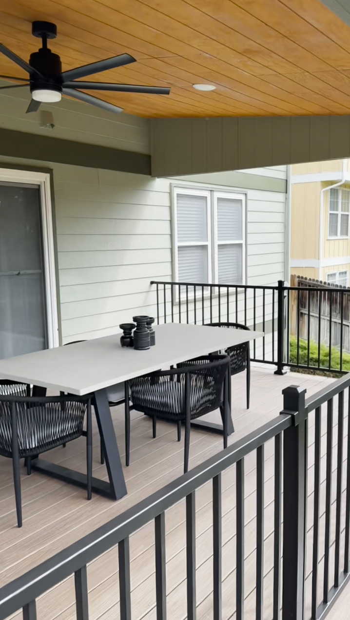Covered porch with black railings, gray table and chairs, ceiling fan, and a camera on the table.
